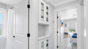 A hallway with white doors, a patterned floor, and a view of a balcony with blue chairs.