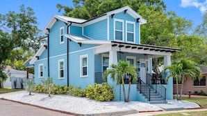 A two-story house with a porch, a staircase, and a small garden with palm trees.