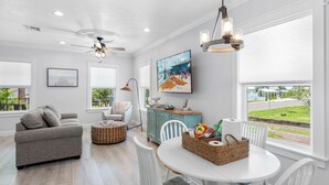 A bright living room with a gray sofa, a white dining table, and a ceiling fan.
