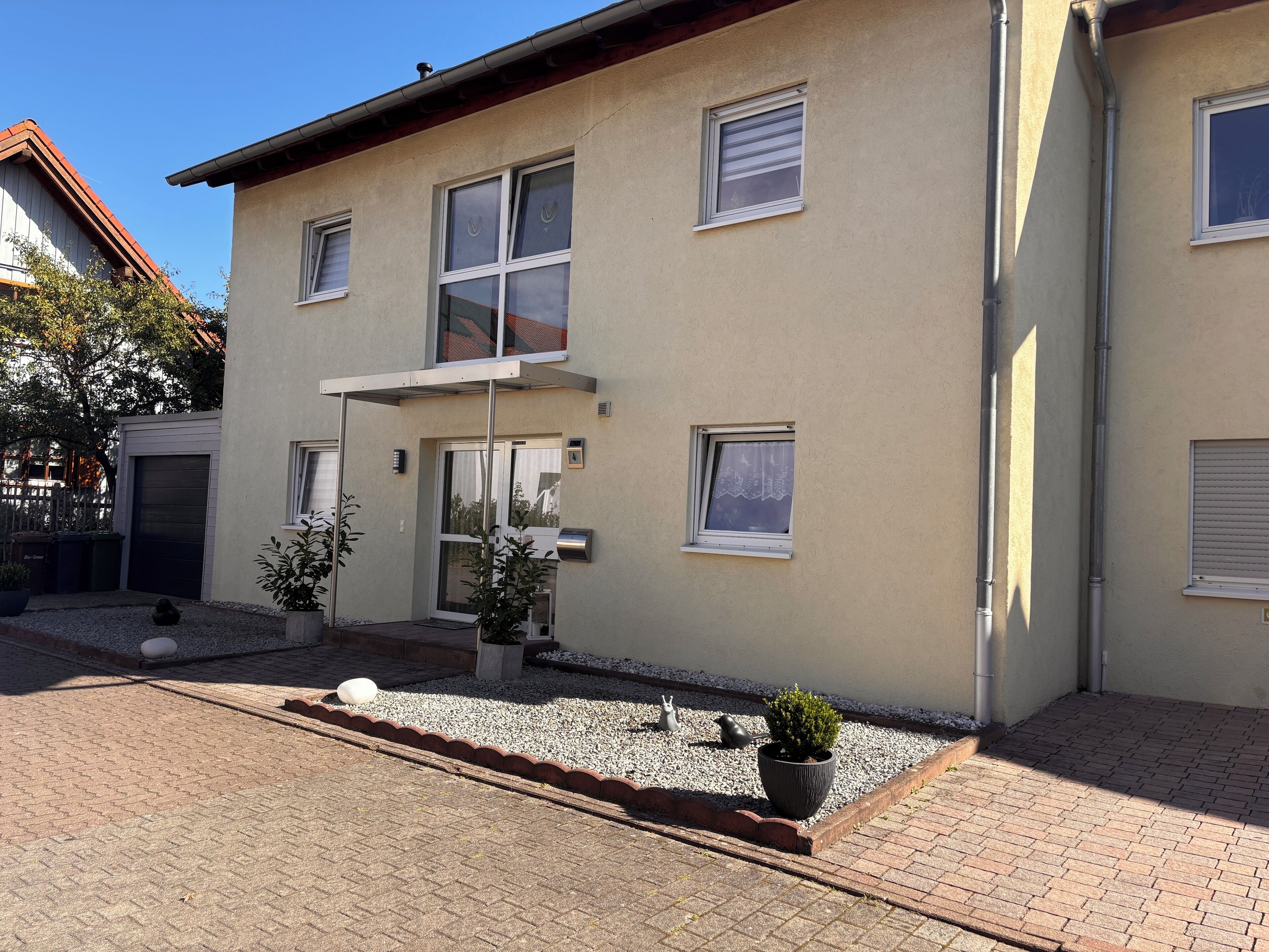 A two-story building with a garage, a small garden with potted plants, and a gravel driveway.
