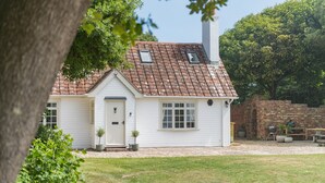 Een wit huis met een rood pannendak, een bakstenen muur en een tuin met een bankje en een barbecue.