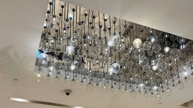 Un hall d’accueil d’hôtel avec un lustre moderne, un comptoir d’accueil et un réceptionniste.