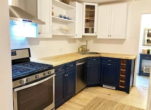 Une cuisine avec des meubles blancs, une cuisinière en acier inoxydable, un lave-vaisselle et un plan de travail en bois.