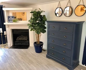 Une pièce avec une cheminée, une commode bleue et une plante en pot.