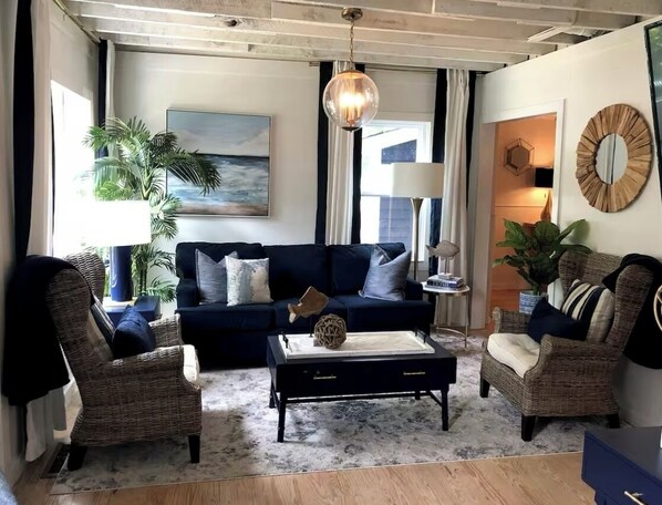 Un salon avec un canapé bleu foncé, deux fauteuils en osier, une table basse et un luminaire suspendu.