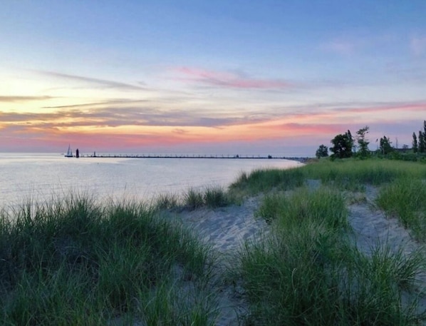 Un paysage côtier avec un pont, des dunes herbeuses et une étendue d’eau calme.