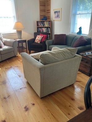 Uma sala de estar com sofá, poltrona, estante de livros e abajur.