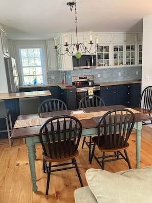 Uma cozinha com mesa de jantar, cadeiras, lustre, armários e micro-ondas.