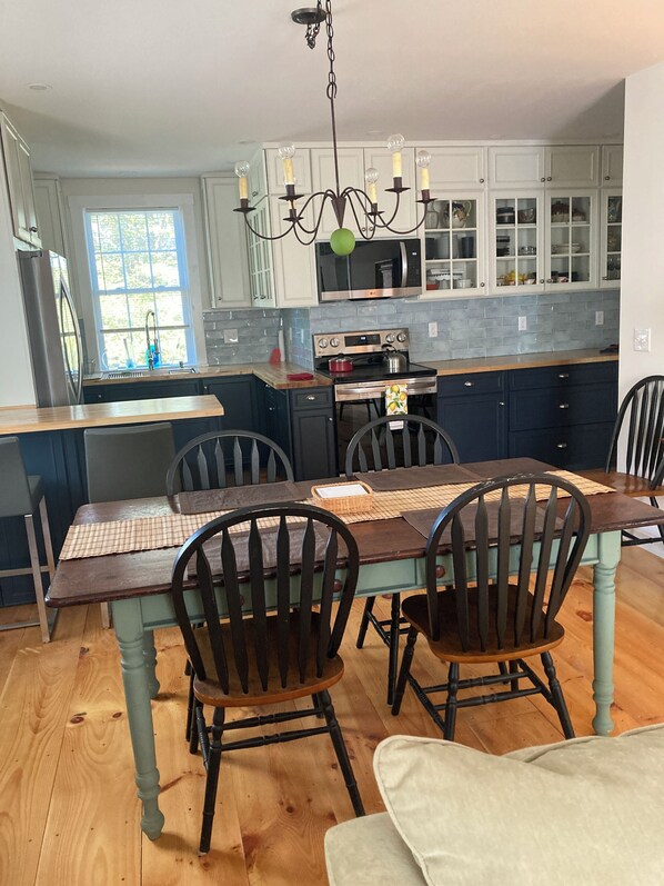 Una cocina con una mesa de comedor, sillas, una araña, armarios y un microondas.
