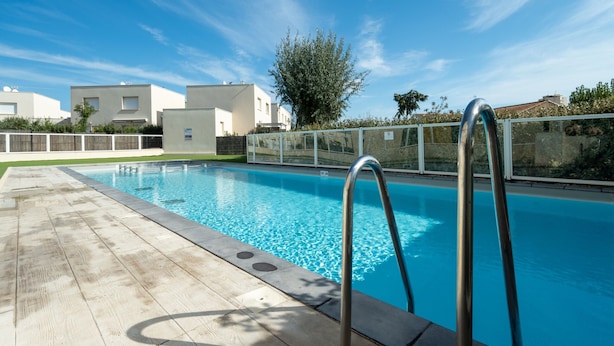 A swimming pool with a wooden deck and metal ladder, surrounded by a white fence and greenery. - Apartment in Valras Plage With View (Sérignan)