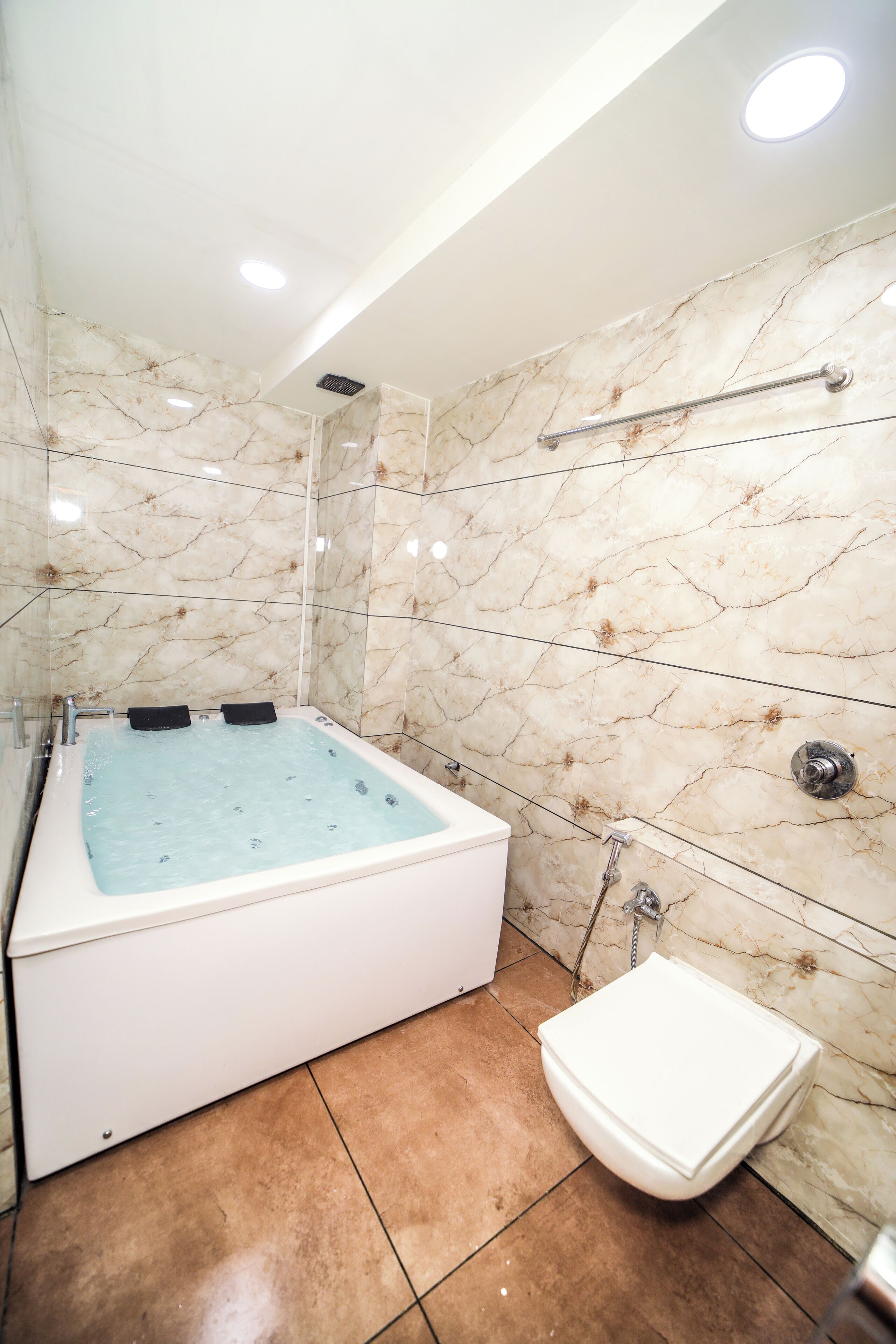 A modern bathroom with a marble wall, a bathtub, a toilet, and a shower.