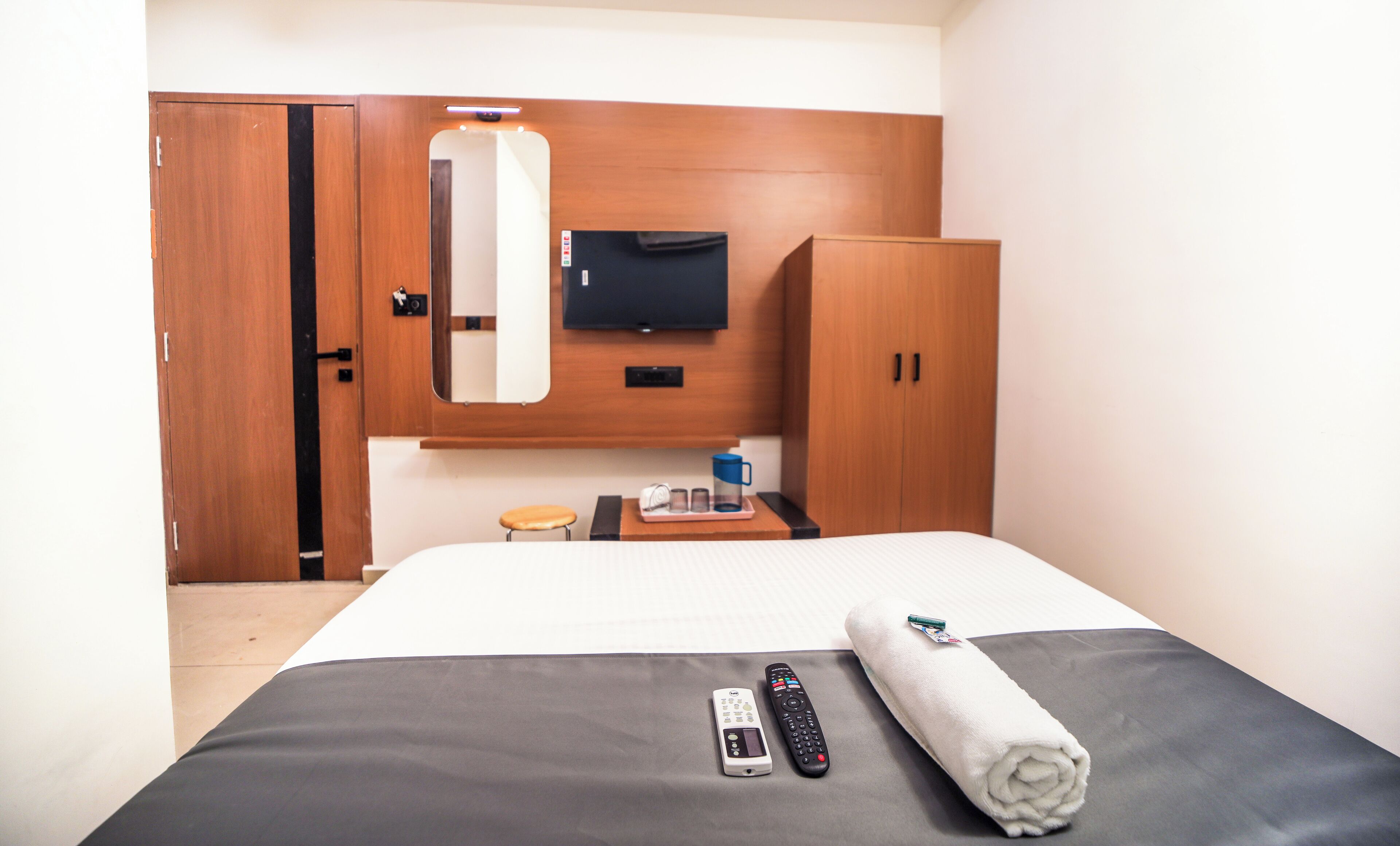 Ein Hotelzimmer mit Bett, Wandfernseher, Holzschrank und kleinem Tisch mit Tablett.