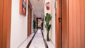 A hallway with wooden doors, a marble floor, and potted plants. - HOTEL NEST ICON  (Ahmedabad)