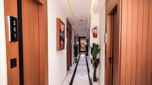 A hotel corridor with wooden doors, numbered room signs, a fire extinguisher, and a marble floor. - HOTEL NEST ICON  (Ahmedabad)