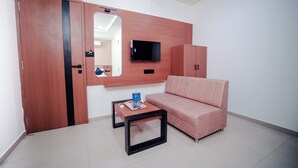 A room with a wooden wardrobe, a television mounted on the wall, a pink sofa, and a small table with a cup and a remote control. - HOTEL NEST ICON  (Ahmedabad)