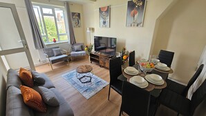 Un salon moderne avec un canapé, un téléviseur, une table à manger et des œuvres d’art accrochées aux murs.