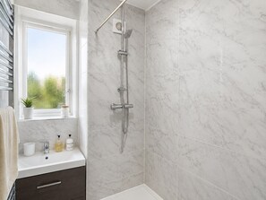 A bathroom with a shower, a window with a view, a sink with toiletries, and a towel rack.