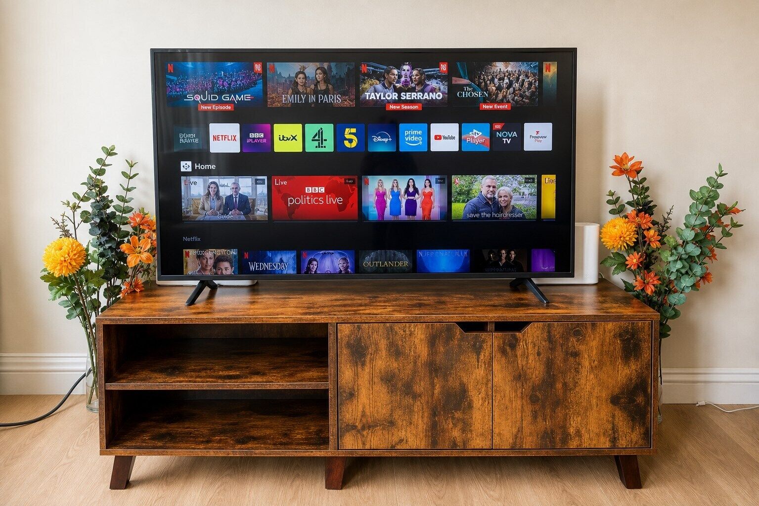A television on a wooden stand with a Netflix interface, surrounded by decorative flowers.