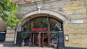 L’entrée d’un restaurant, avec une grande fenêtre en arc de cercle et une enseigne indiquant « Nando’s ».