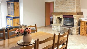 A dining area with a wooden table and chairs, a vase of flowers, and a stone fireplace with a TV above it. - Comfort villa on the lake (VINS SUR CARAMY (83170))