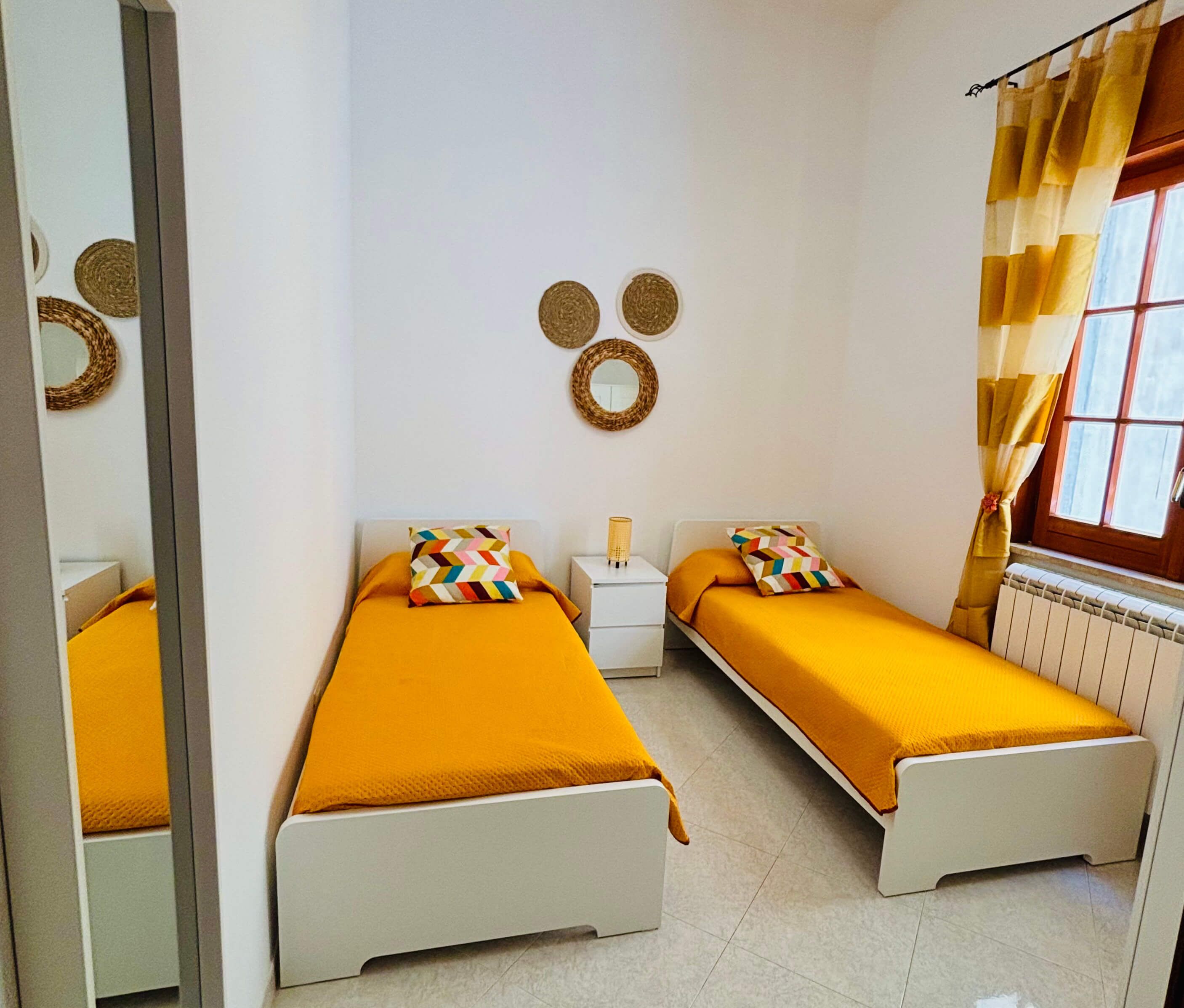 Un dormitorio con dos camas, un espejo, una mesita de noche y una ventana con cortinas.