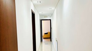 A corridor with a wooden door on the left, a radiator on the right, and a bed in the distance.