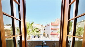 A balcony with a table and chairs, a potted plant, and a view of buildings and palm trees.