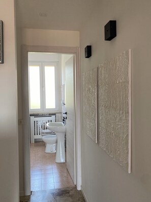 A hallway leading to a bathroom with a sink, toilet, and window. - Jaris Apartment (Vicenza)