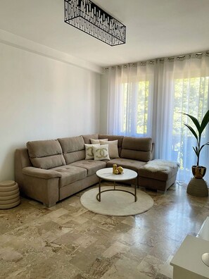 A living room with a beige sectional sofa, a round coffee table, and a potted plant. - Jaris Apartment (Vicenza)