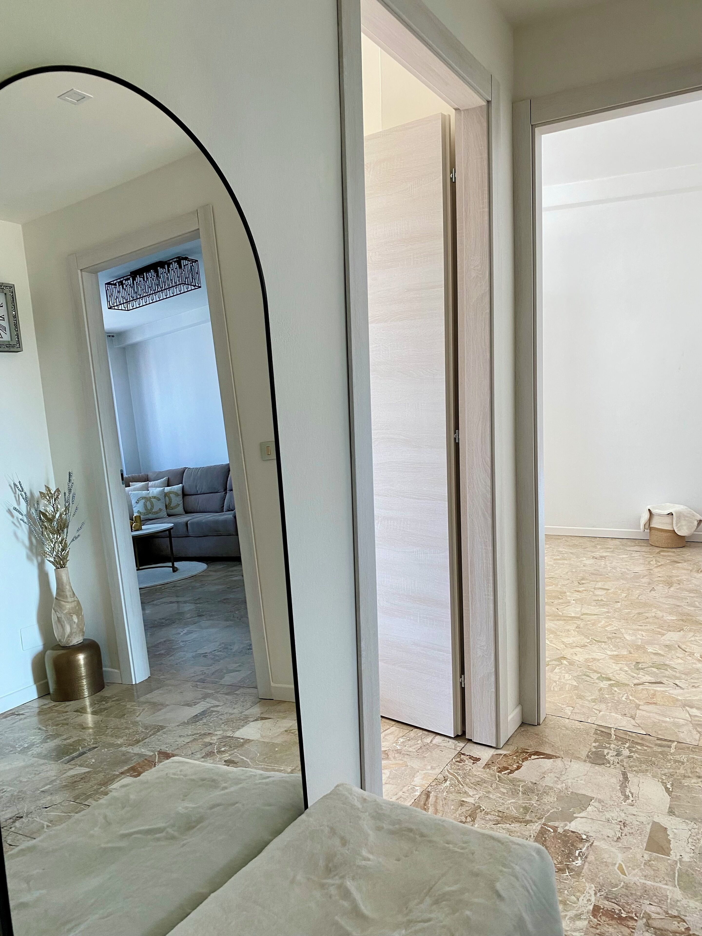Ein modernes Interieur mit einem großen Spiegel, der in einen Wohnbereich reflektiert, einem Steinboden und einer Tür zu einem anderen Raum.