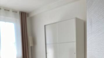 A hotel room with a bed, a wardrobe, and a wall-mounted control panel.