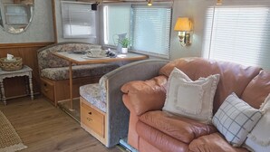 A compact RV interior with a kitchenette, a seating area with a cushioned couch, a small table with a plant, and a wooden floor. - Garden vibe stationary RV in No.
 San Diego County with WiFi, AC. TV. Views. (Escondido)