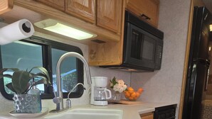 A compact kitchen with wooden cabinets, a microwave, a coffee maker, and a sink. - Garden vibe stationary RV in No.
 San Diego County with WiFi, AC. TV. Views. (Escondido)