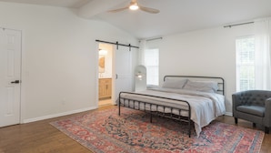 Une chambre à coucher avec un lit, un ventilateur de plafond, une chaise et un tapis à motifs.