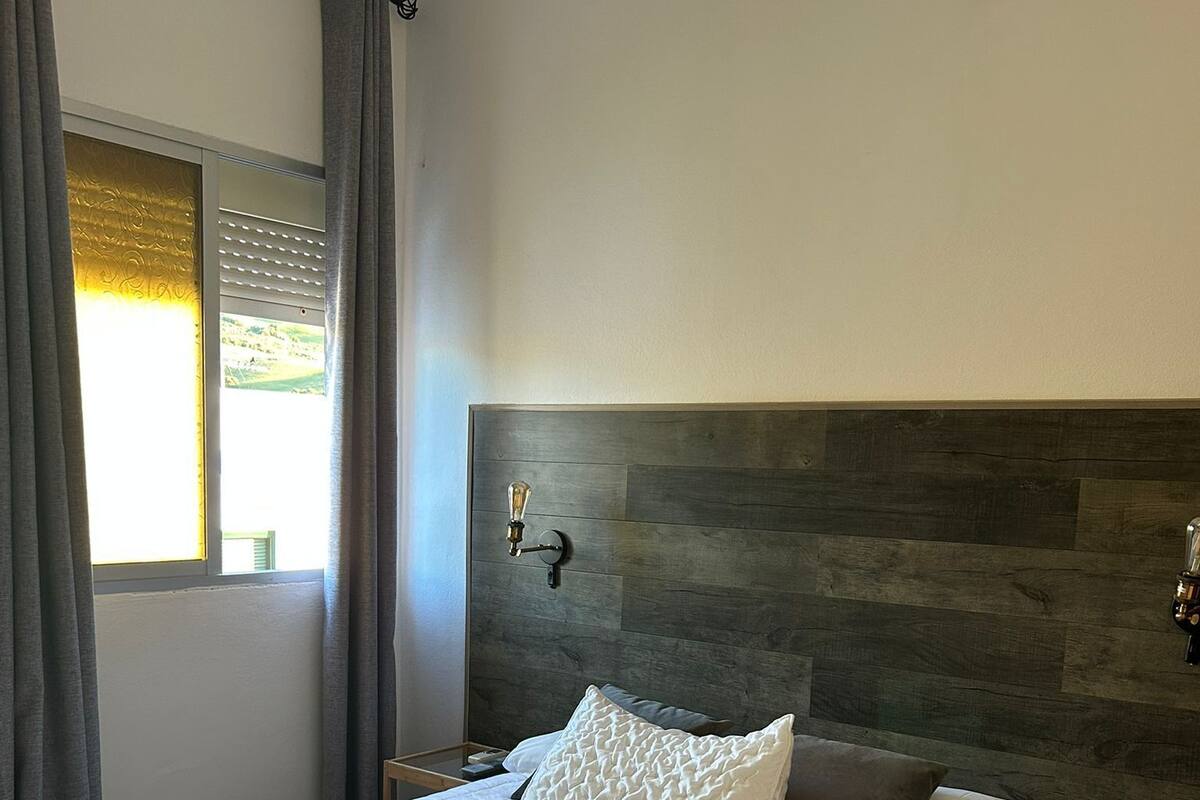A large bed with white linens, a wooden headboard, and a bedside lamp.