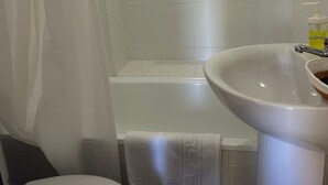 A bathroom with a white toilet, a sink with a soap dispenser, and a shower area. - Hostal El pinar (Montecorto)