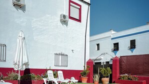 A swimming pool with lounge chairs and a red and white building in the background. - Hostal El pinar (Montecorto)