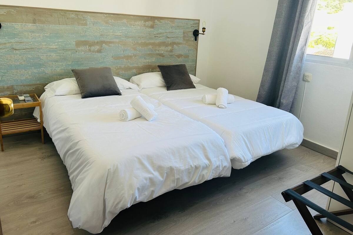 A double bed with white linens, a wooden headboard, and a bedside table with a lamp.