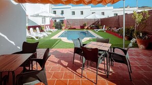 An outdoor patio with a pool, surrounded by white buildings, under a large orange canopy. - Hostal El pinar (Montecorto)