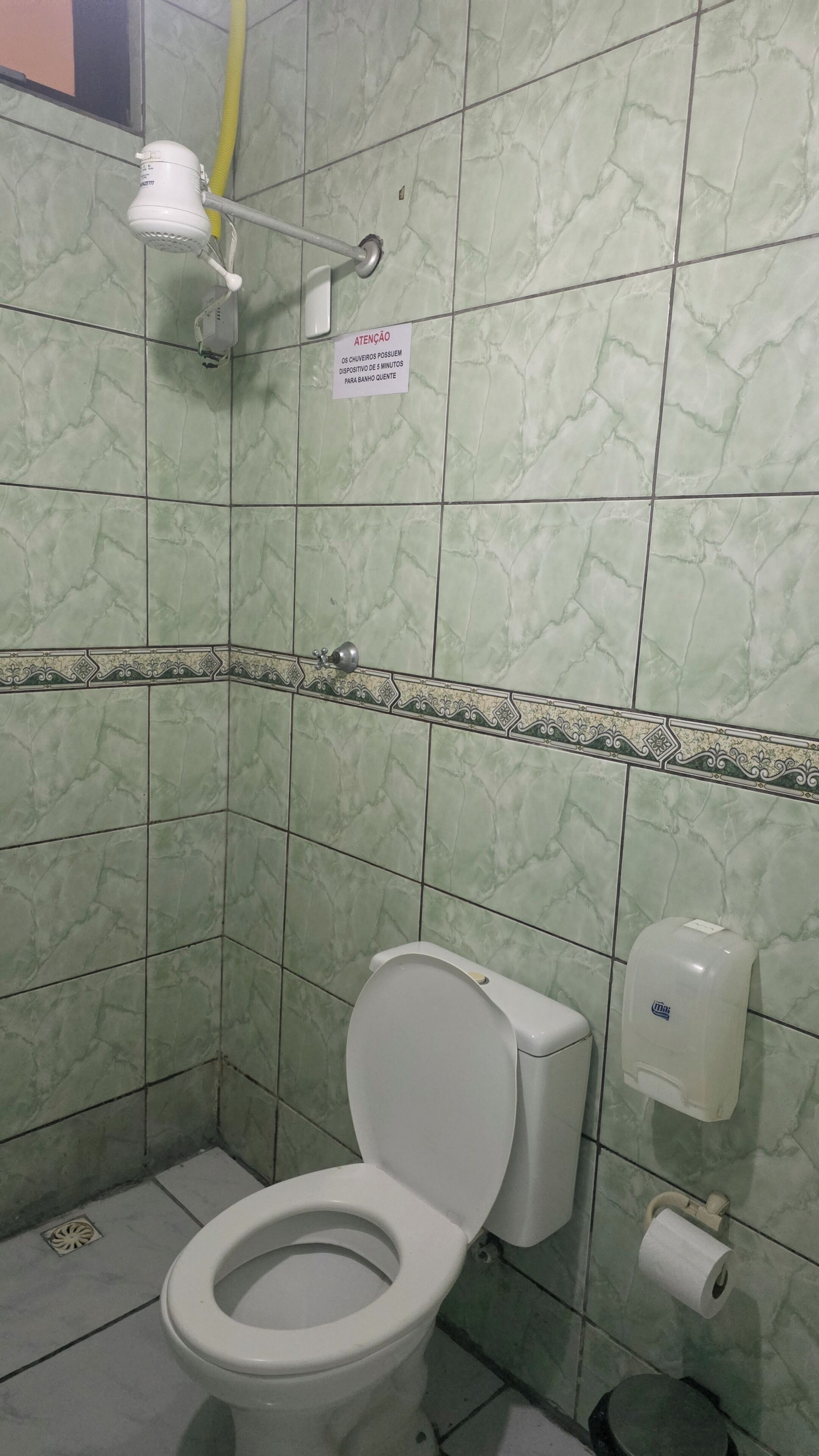 Une salle de bain équipée de toilettes, d’un sèche-mains et d’un distributeur de serviettes en papier.