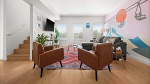 Un salon moderne avec un escalier, un canapé, une table basse et une fresque murale colorée.