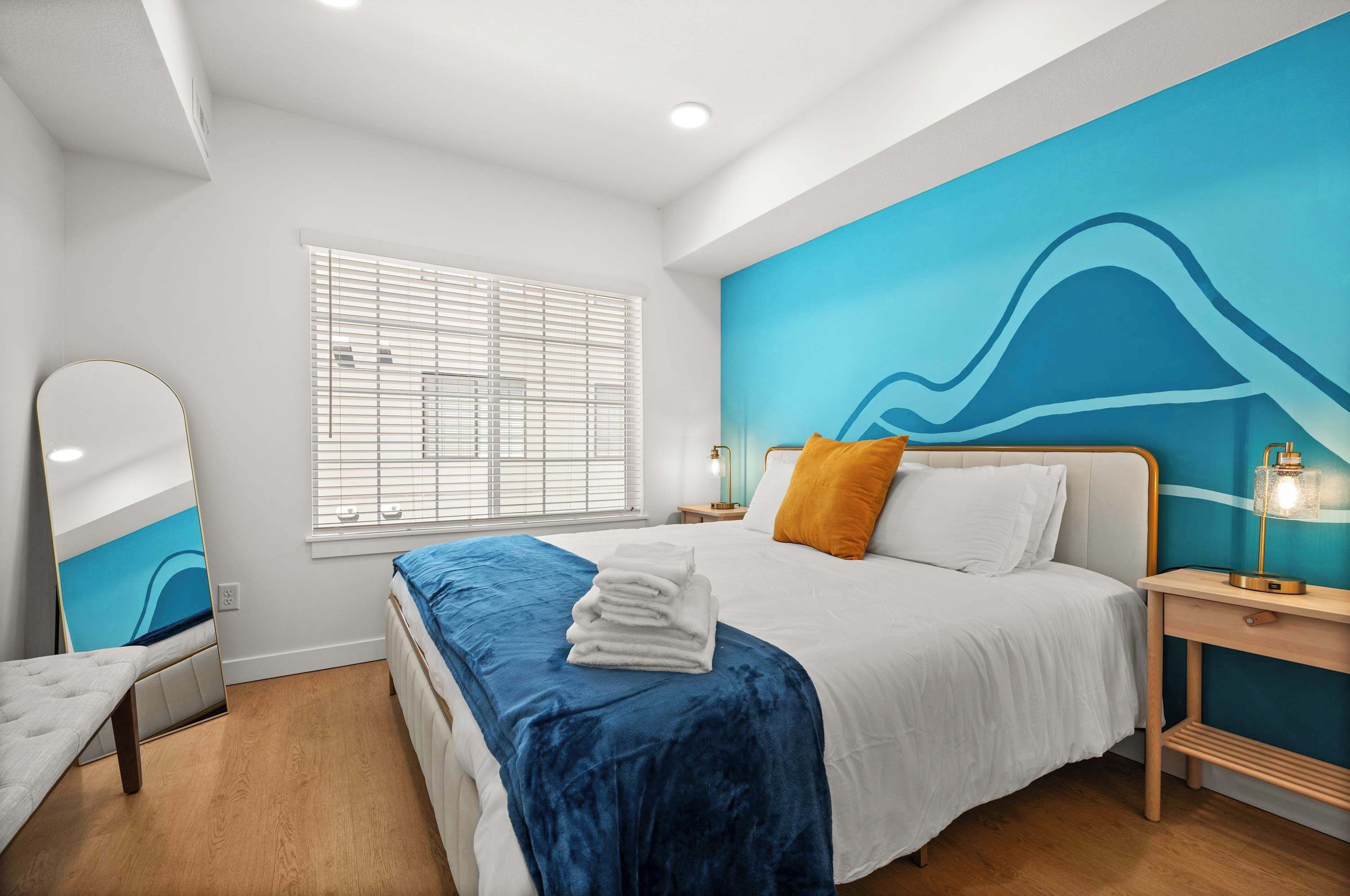 Quarto moderno com cama, mesa de cabeceira, espelho e janela com persianas.