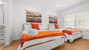 Hotelkamer met twee bedden, witte lakens, oranje plaids, houten hoofdeinden en wanddecoratie.