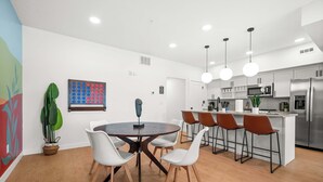 Een moderne keuken met roestvrijstalen apparatuur, een centraal eiland met barkrukken, en een eetgedeelte met een ronde tafel en stoelen.