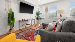 Un salon moderne avec un canapé gris, un fauteuil jaune et un téléviseur à écran plat fixé au mur.