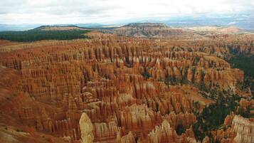 A vast canyon landscape with rugged, layered rock formations and distant mountains under a cloudy sky.