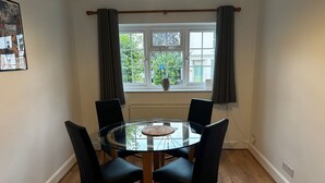 Een eetgedeelte met een ronde glazen tafel, vier zwarte stoelen en een raam met gordijnen.