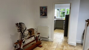 Een hal met een houten schommelpaard, een radiator en een keuken zichtbaar door een geopende deur.