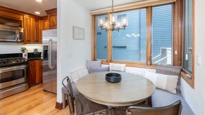A kitchen with wooden cabinets, a stainless steel refrigerator, a microwave, and a stove. There is a dining table with chairs and a chandelier above it.