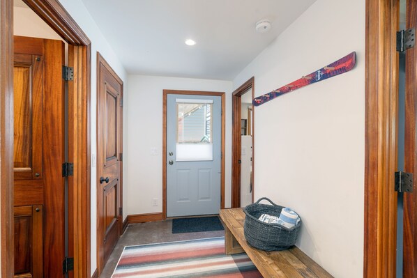 Un pasillo con puertas de madera, un banco, un perchero para esquíes en la pared y una puerta con panel de vidrio esmerilado.